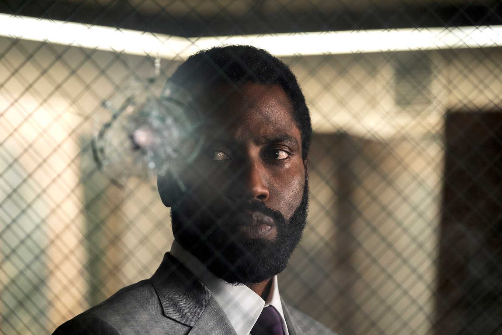 John David Washington standing in front of a bullet wound in bulletproof glass in Tenet