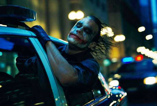 Heath Ledger as The Joker sticks his head out the window of a car racing down the streets in The Dark Knight.